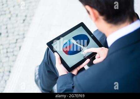 Businessman checking a pie graph on a tablet computer navigating the touchscreen with his finger as he sits on a street in town Stock Photo
