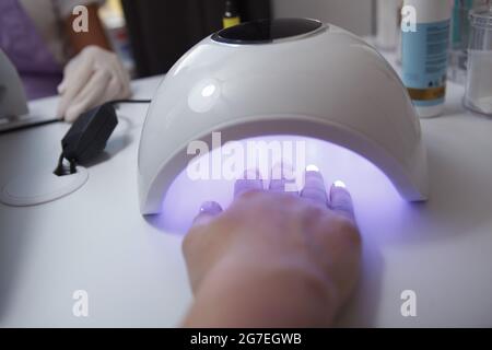 Cropped close up of a hand with fresh manicure drying in uv lamp at nail salon Stock Photo