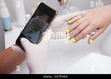 Close up of manicurist taking photos of clients nails with her smart phone after manicure Stock Photo