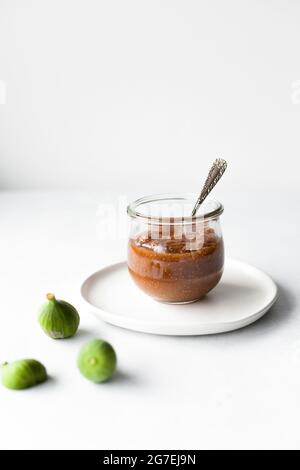 Fig jam jar with a spoon and fresh figs on a white surface. Stock Photo