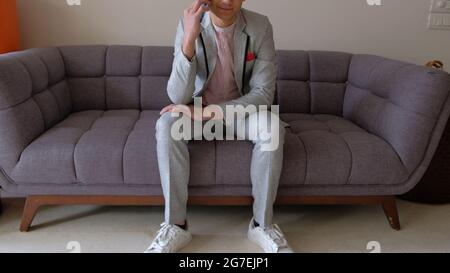 Young Indian male in an elegant suit talking on the phone while sitting on the couch Stock Photo