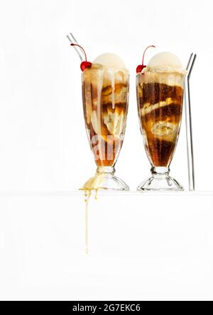 Two root beer floats in classic milkshake glasses floating on a glass surface with drips. White background. Stock Photo