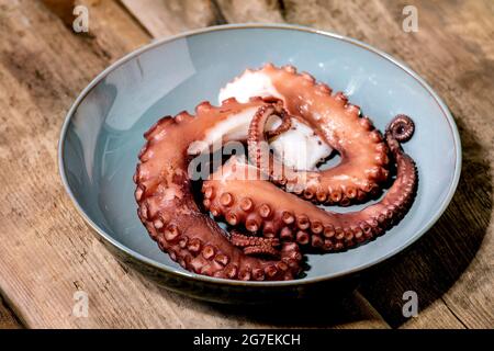 Cooked tentacles of octopus on blue ceramic plate over brown wooden background Stock Photo