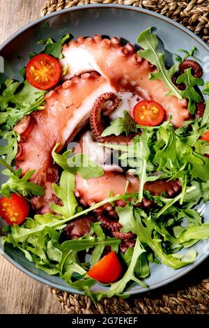 Seafood salad. Cooked tentacles of octopus on blue ceramic plate served with rocket leaf aragula and cherry tomato salad Stock Photo