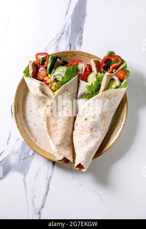 Traditional mexican tortila wrap with pork meat and vegetables in ceramic plate over white marble background. Top view, flat lay. Homemade fast food Stock Photo