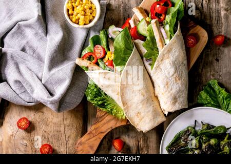 Traditional mexican tortila wrap with pork meat and vegetables on wooden cutting board decorated with white textile napkin corn and grilled jalapenos Stock Photo