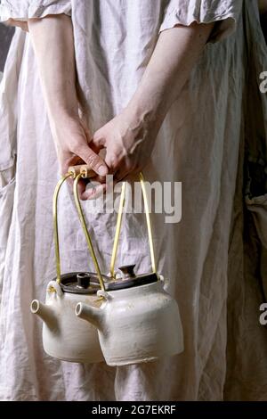 Female in white cotton dress holding two white handmade ceramic teapots for traditional Japanese tea ceremony. Teadrinking Stock Photo