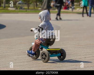 A boy learns to ride a tricycle in the park on a sunny weekend. Stock Photo