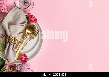 Elegant table setting with floral decor, flat lay. Wedding or festive table setting. Plate and cutlery with pink flowers on pink background Stock Photo