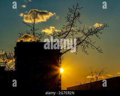 The rays of the setting sun between the houses of a large industrial city. Stock Photo