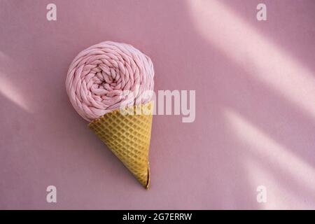 Top view of pink macrame yarn skein in ice cream waffle cone on a pink background with sunlight beams Stock Photo