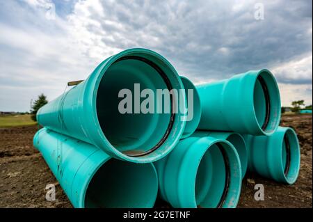 Stacked water main pipe with bell fitting next to an exposed trench for installation Stock Photo