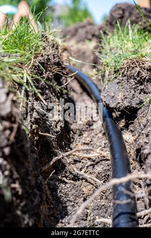 Focus on a black 1 inch sprinkler plastic water line laid in a shallow trench Stock Photo