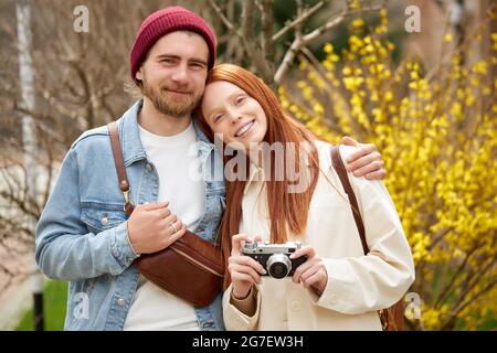 married couple travelers in casual wear walk in spring or autumn forest, with retro camera, taking photo of sights around, in contemplation. portrait Stock Photo