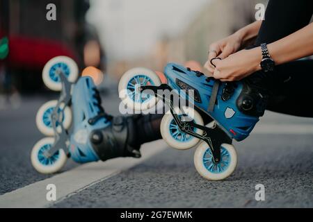 Horizontal shot of faceless woman puts on rollerskates rides on road poses against urban background involdved in active sport. People hobby recreation Stock Photo
