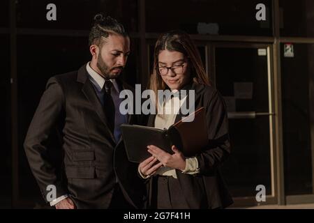 Hispanic professional-looking male and female standing outside a building and reading a book Stock Photo