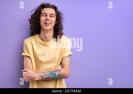 Positive Brunette Guy With Long Curly Hair Laughing, Standing With Arms Folded. Man Is In Good Mood, Happy Guy In Casual Wear Enjoys Life Stock Photo