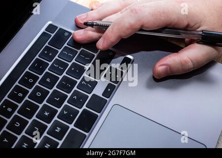 Hands Pressing Computer Keyboard Keys While Writing With Pencil In Notepad. Palms Typing Notebook Keypad And Writing Pencil Over Paper. Stock Photo