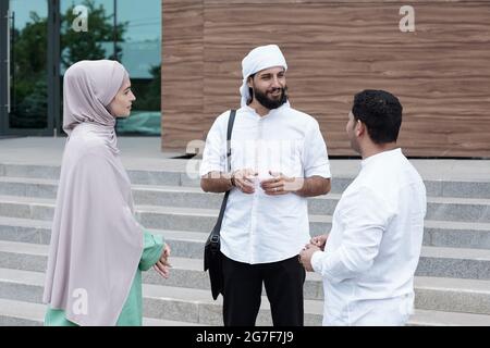 Group of Islamic students standing in circle and discussing project ideas after classes Stock Photo