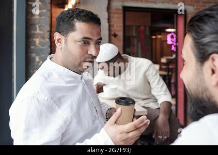 Middle-aged Arabian man gestuing hand while talking to friend and drinking coffee in cafe Stock Photo