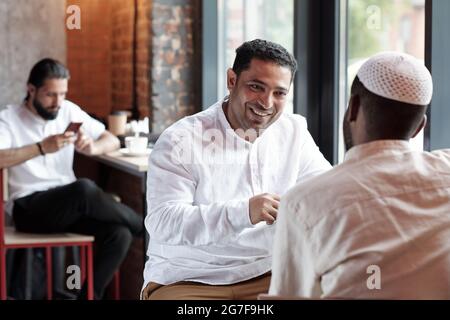 Positive Muslim men sitting at counter in cafe and chatting together Stock Photo