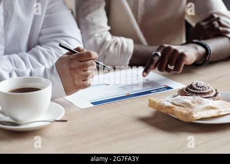 Close-up of unrecognizable men sitting at table with pastry on plate and analyzing bill together Stock Photo