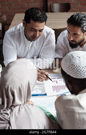 Group of concentrated team of business specialists sitting at table and discussing graph changes Stock Photo
