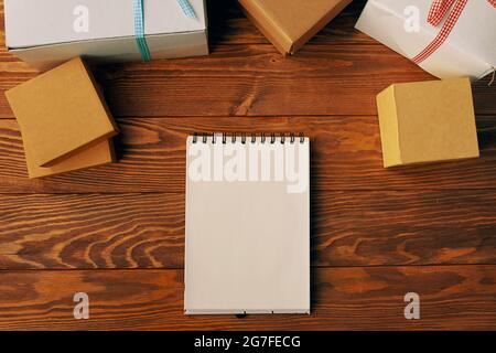 Top view of blank spiral bound notebook and gift boxes on wood table background. Business desk minimal style concept with copy space for any design. Christmas New Year and other holidays concept. Stock Photo