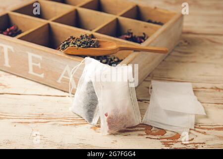 Tea bags and box with dry leaves on light wooden background Stock Photo