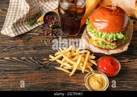 Tasty french fries, burger and glass of beverage on wooden background Stock Photo