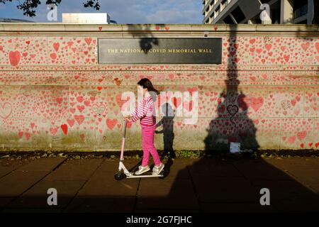 A young girl riding a scooter passes the National Covid Memorial Wall on London's Southbank, close to St Thomas' Hospital.