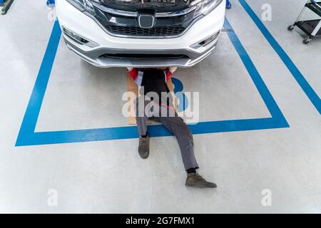 Top view of mechanic in uniform lying down and working under car, car mechanic adjusting tension in vehicle suspension Element at auto repair service Stock Photo