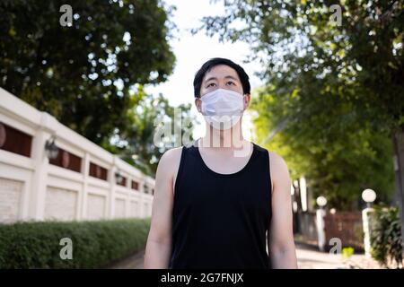 Young Asian man running with a face mask in the city. Male runner exercising and jogging on the street Stock Photo
