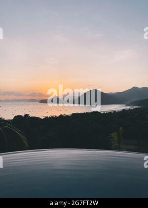 Luxury infinity pool overlooking tropical beach lagoon during sunset time Stock Photo