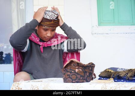 Pasuruan, Indonesia. June 2021. A man is putting Udeng on his head. Udeng is a batik cloth tied to the head for decoration of the Tenggerese and Javan Stock Photo