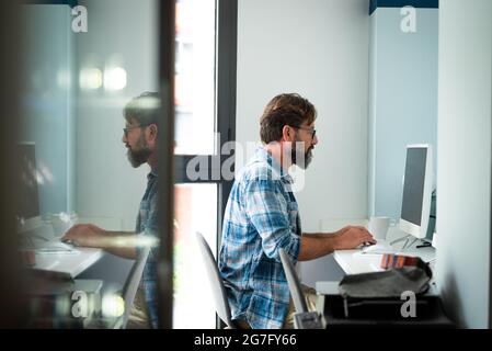 Caucasian freelance people man sitting at the desk typing on desktop computer for online job internet connected lifestyle - hipster adult male working Stock Photo