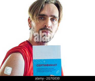 A man after vaccination with a patch pasted on his shoulder holds a vaccination certificate in his hand. Translation: certificate of vaccination again Stock Photo