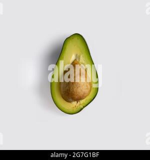 Half a green ripe avocado fruit with stone inside. Isolated on light-gray background. Flat lay, top view Stock Photo