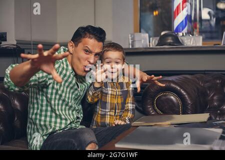 Young father and his stylish little son in the barbershop in the waiting room. Stock Photo