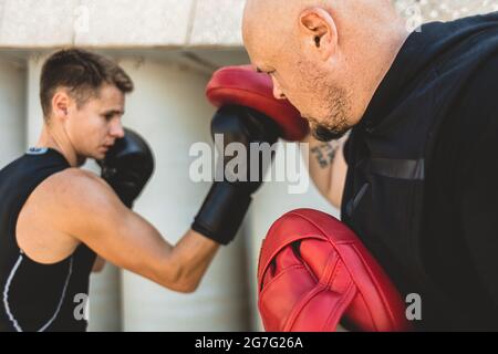 Two men exercising and fighting in outside. Boxer in gloves is training with a coach Stock Photo