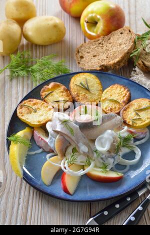 Salty herring fillets with apple slices and sour cream sauce, served with crispy baked rosemary potatoes Stock Photo