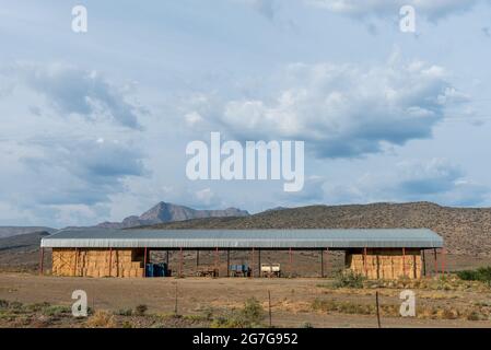 KLAARSTROOM, SOUTH AFRICA - APRIL 21, 2021: A farm shed with bales of hay and trailers next to road R407 near Klaarstroom Stock Photo
