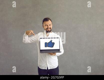 Happy young man pointing at a thumbs up symbol on the screen of his laptop computer Stock Photo