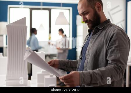 Architect adult man looking at blueprint plan in office place to work on modern design building model. Caucasian businessman inspecting sketch development project construction Stock Photo