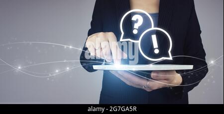 FAQ frequently asked questions concept. White tablet in businesswoman hand with digital hologram FAQ question answer sign on grey background. Quiestio Stock Photo