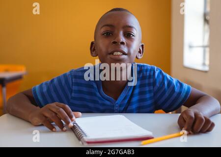 Portrait of african american schoolboy sitting at desk with notebook ...