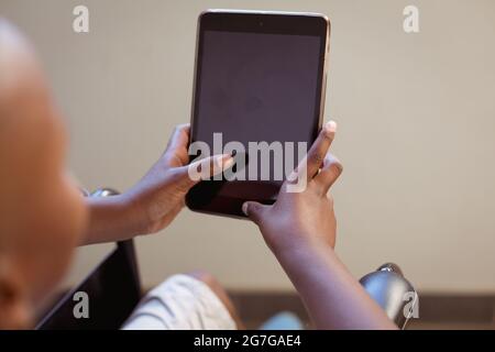 Disabled african american schoolboy sitting in wheelchair using tablet, copy space on screen Stock Photo