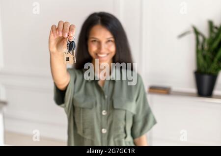 Selective focus on the key in hand of happy young indian woman, cheerful female moved in new house, rent apartment, bought own real estate, the key with keyring in shape of little house Stock Photo