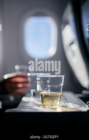 Disposable cups of drinks (water and wine) on table against airplane window. Refreshment during flight. Stock Photo