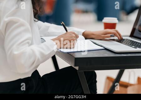close-up. woman using a laptop and taking notes in a notepad Stock Photo